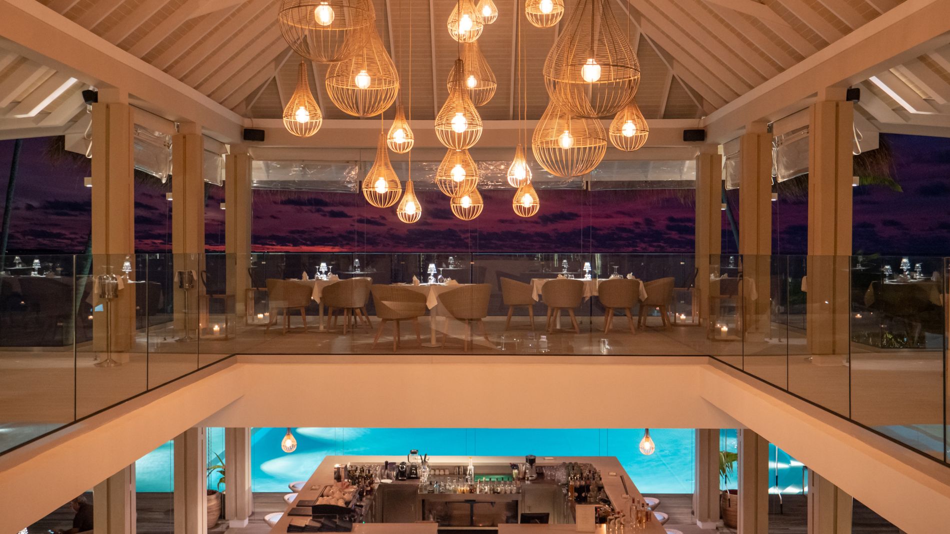Luxuriöses Restaurant im Baglioni Resort Maldives: Oberes Esszimmer mit Hängeleuchten, Glasgeländern, Blick zum unteren Poolbereich.