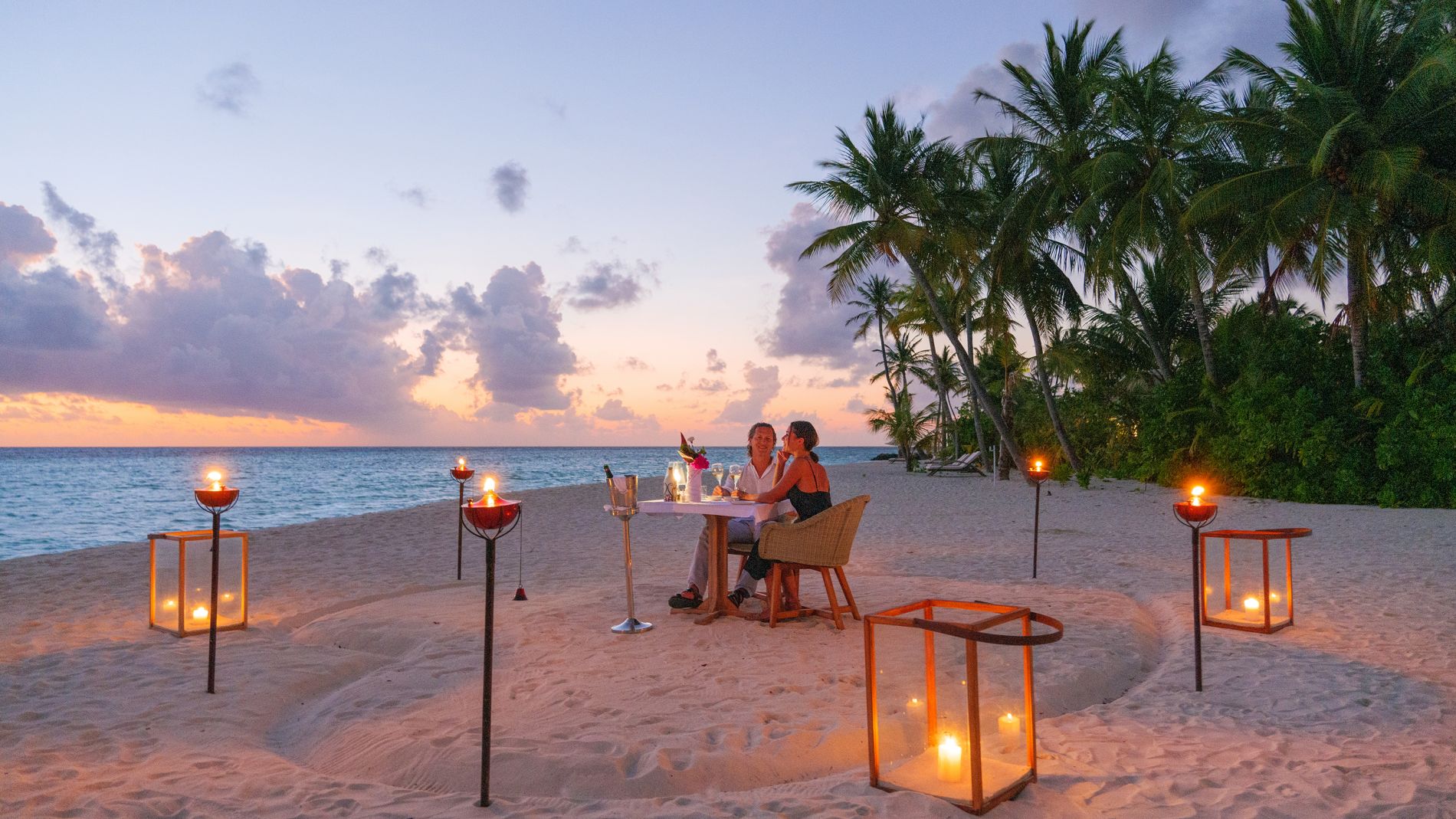 Paar beim Dinner am Strand mit Kerzen, Palmen und Meer, Baglioni Resort Maldives.