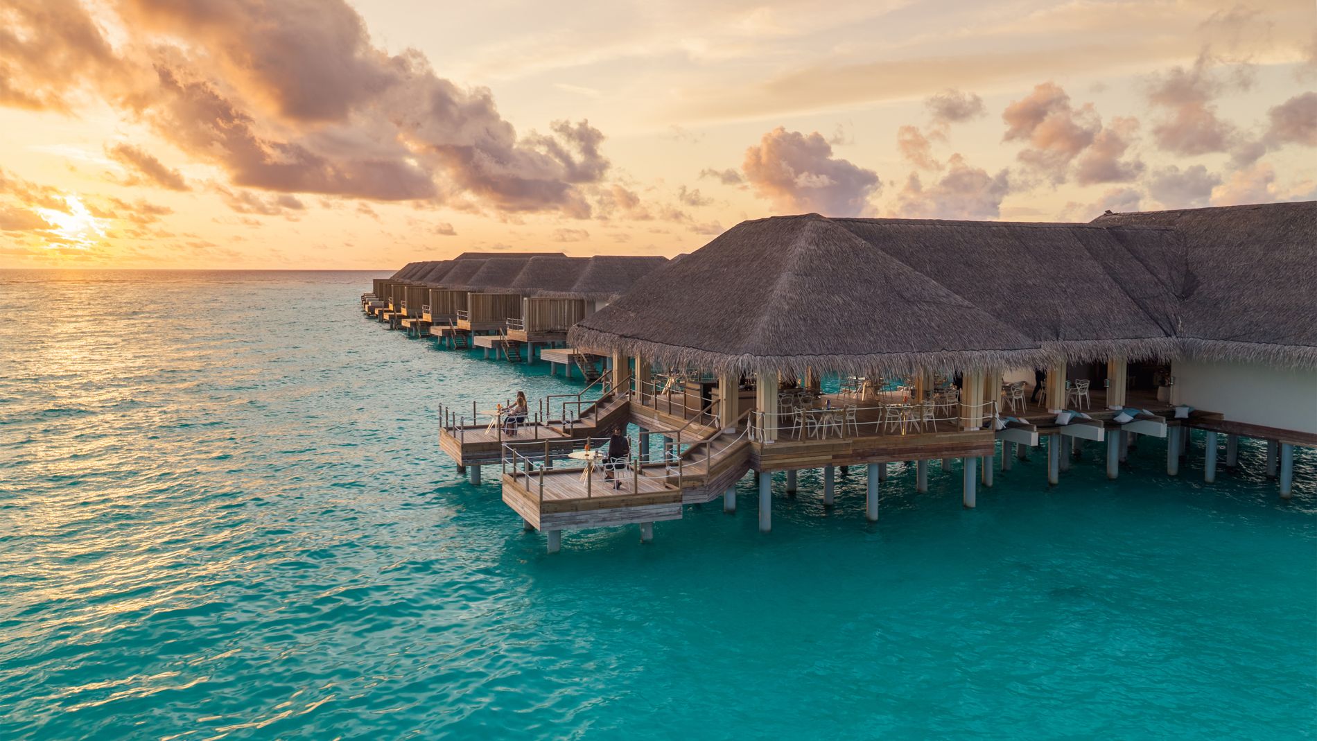 Overwater-Bungalows im Baglioni Maldives bei Sonnenuntergang; türkisblaues Meer, Holzverandas, Strohdächer.