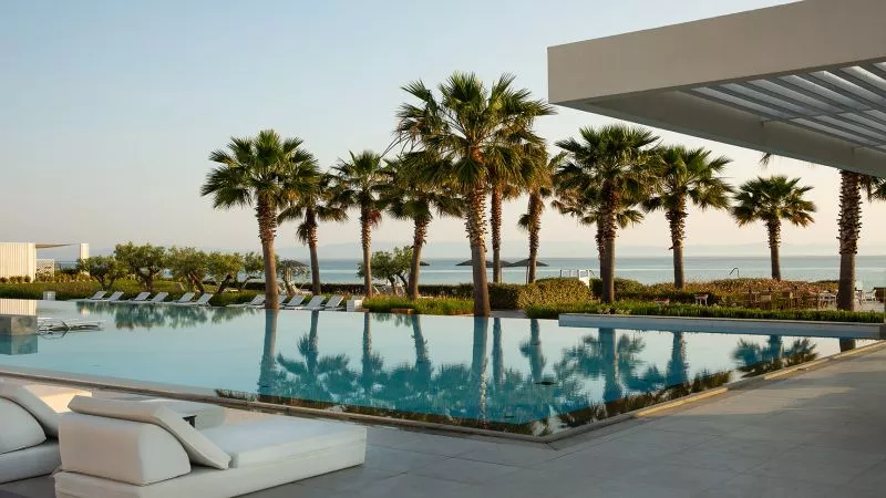 Domes Noruz Kassandra Pool: Pool mit Palmen, Liegen am Beckenrand, Meerblick, modernes Resort am Strand.