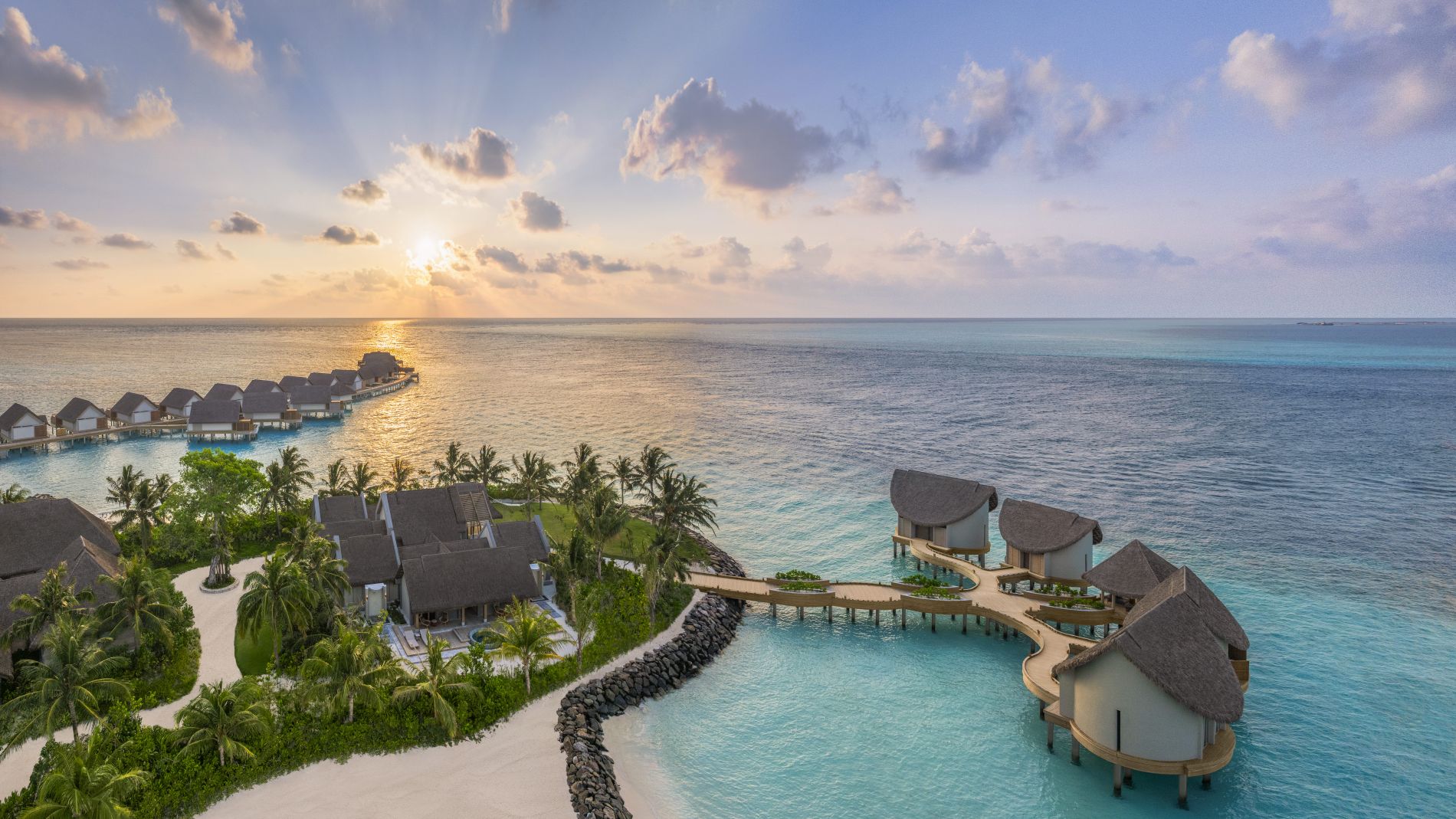 Sonnenaufgang über JW Marriott Maldives Kaafu Atoll Resort mit über dem Wasser schwebenden Bungalows, Palmen und ruhigem Meer.