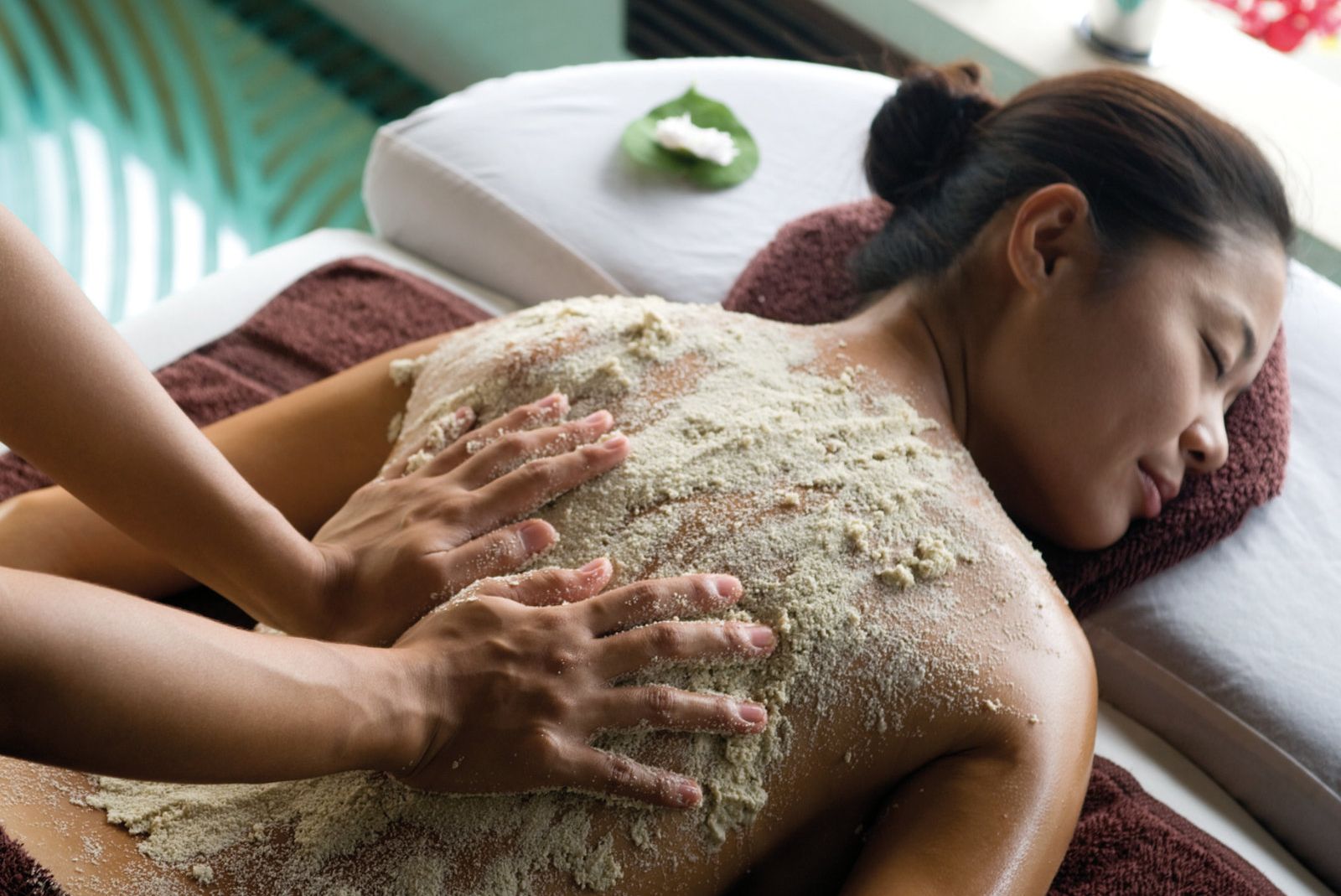 Eine Person erhält eine Körperpeeling-Behandlung in einem Spa, mit Handbewegungen auf dem Rücken.