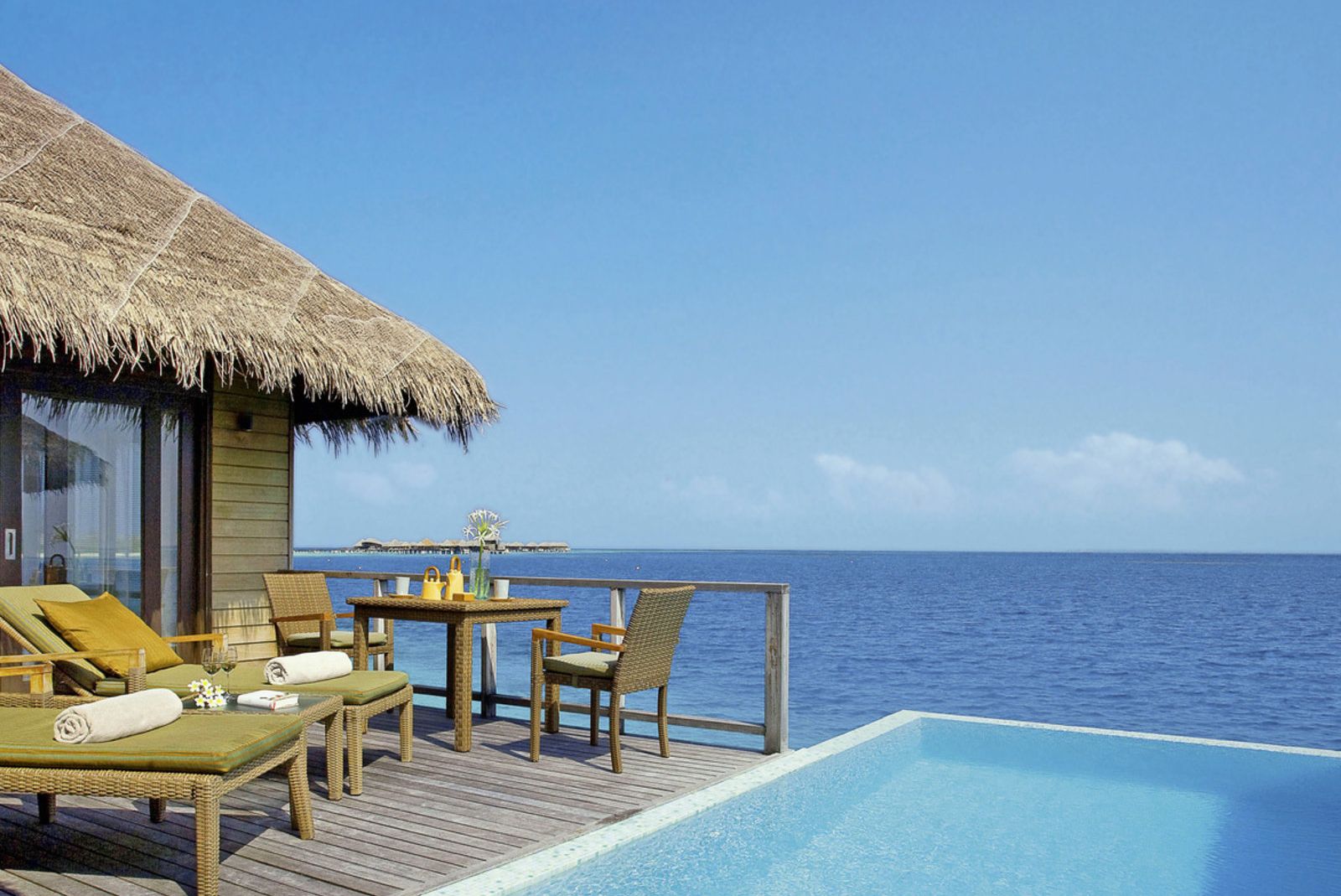 Terrasse mit Liegen und Tisch, Blick auf das Meer und einen Pool, typisch für eine maledivische Unterkunft.