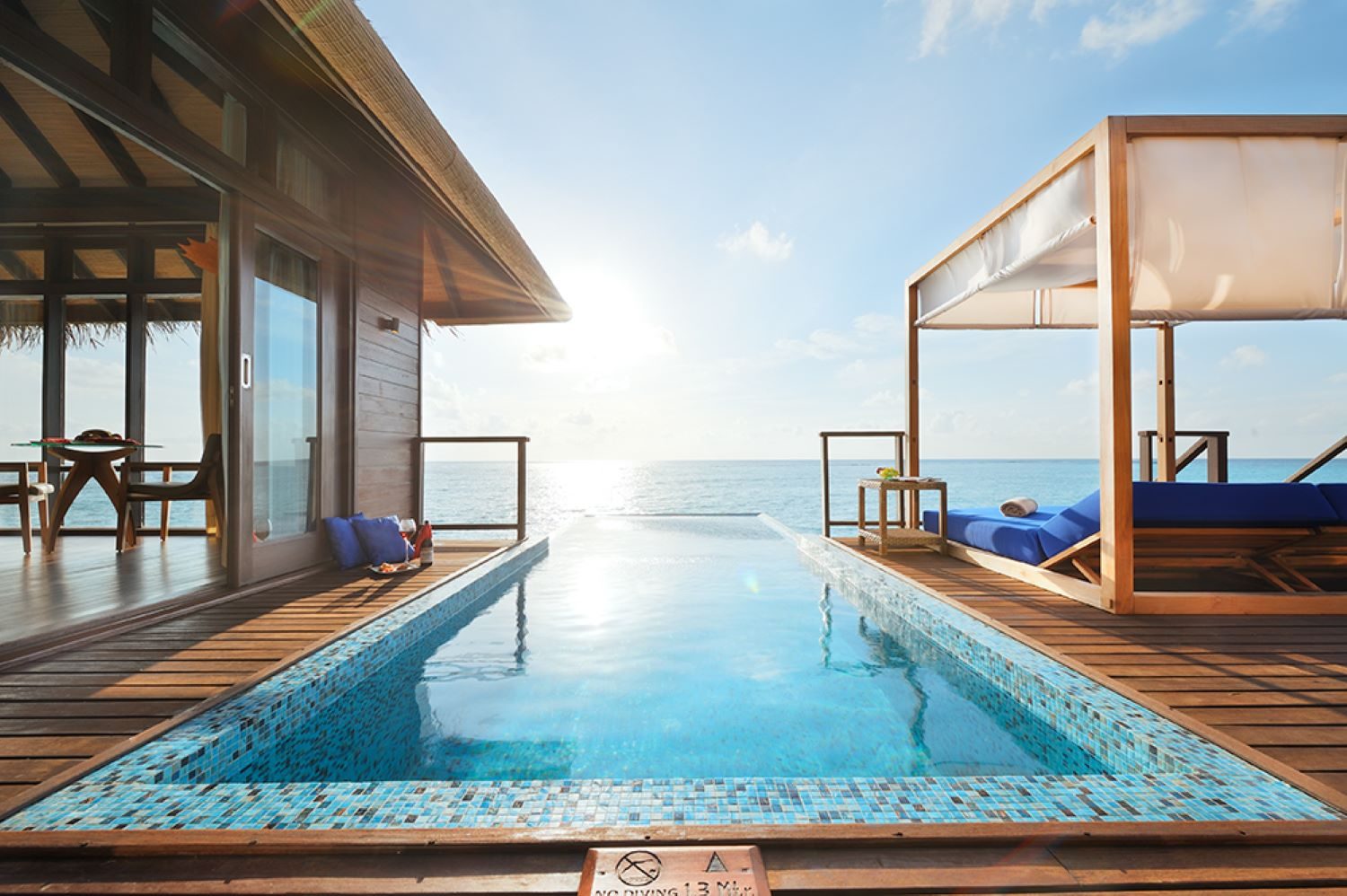 Modernes Überwasserhaus mit Pool, Blick aufs Meer und Sonnenecke, unter strahlend blauem Himmel in Kokosnuss-Resort.