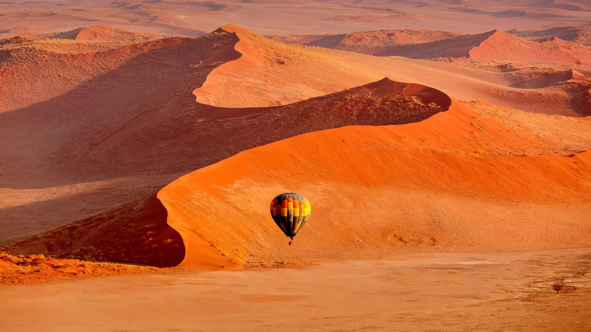 Ein Heißluftballon schwebt über orangefarbenen Sanddünen in Sossusvlei, Namibia, umgeben von einer weiten, trockenen Landschaft.
