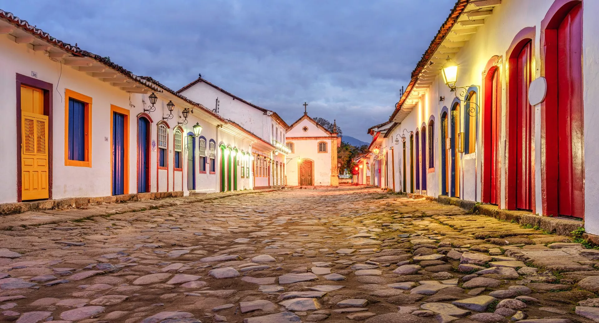 Straße mit bunten Häusern und der Nossa Senhora do Rosário Church in der Dämmerung, umgeben von gepflastertem Boden.
