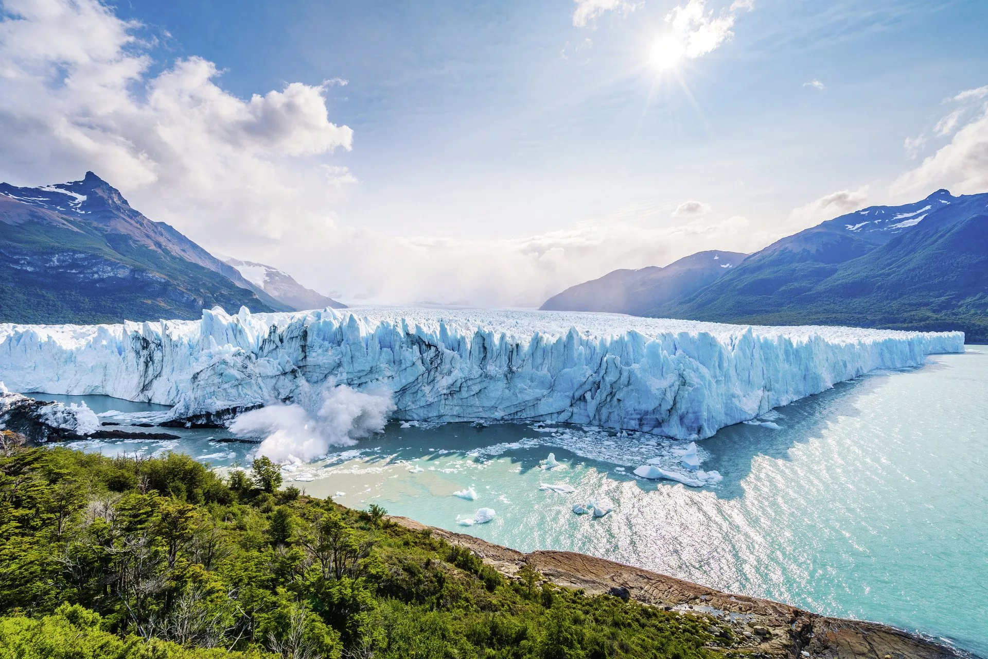 Panoramablick auf den Perito Moreno Gletscher in El Calafate, Patagonia, mit grünen Uferbereichen und Bergen im Hintergrund.